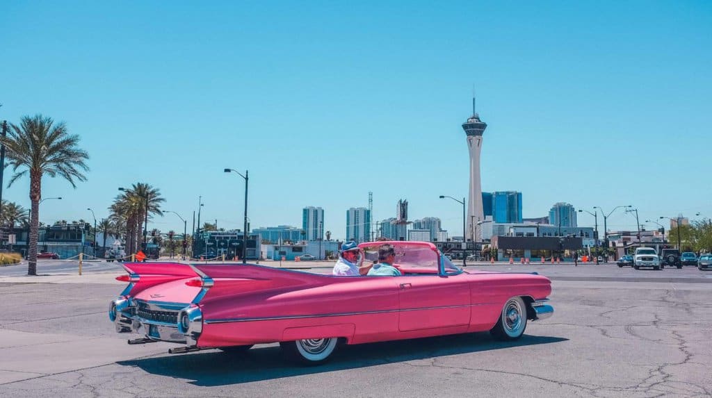A pink classic vintage car with a view of Las Vegas, The Strat Casino and hotel.